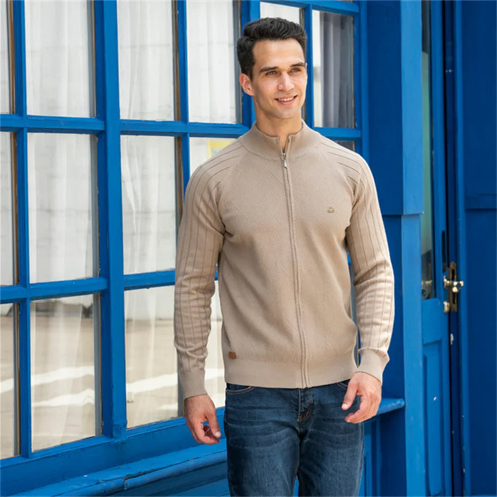 Homme portant le gilet Erik beige devant une fenêtre bleue